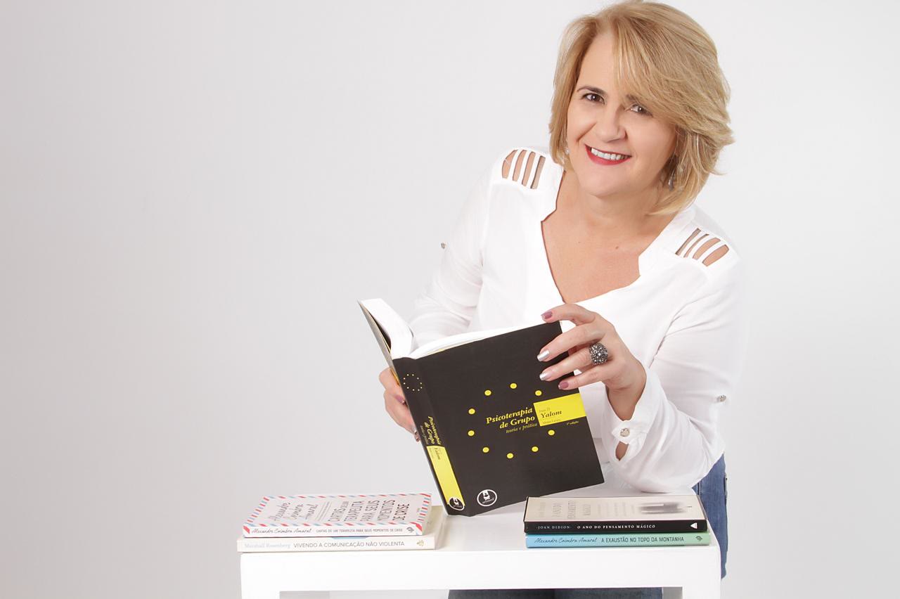Rita Remonato folheando um livro de psicoterapia de grupo, ao lado de outros livros de psicologia