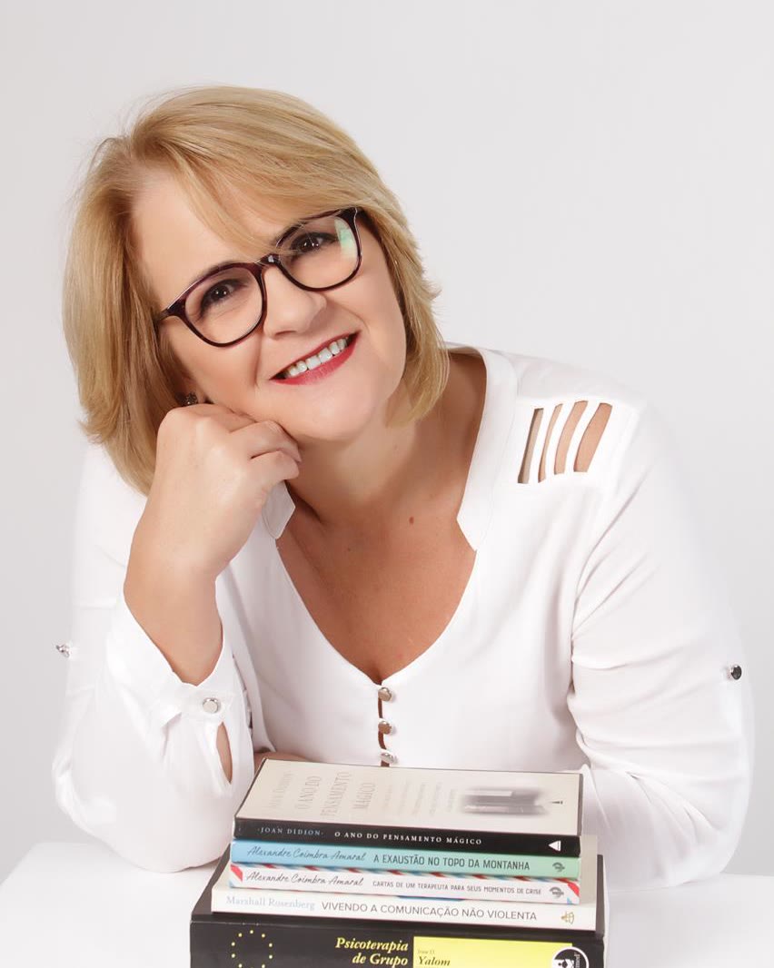 Rita Remonato, psicóloga CRP 12/00823, apoiada em uma mesa com livros de psicologia